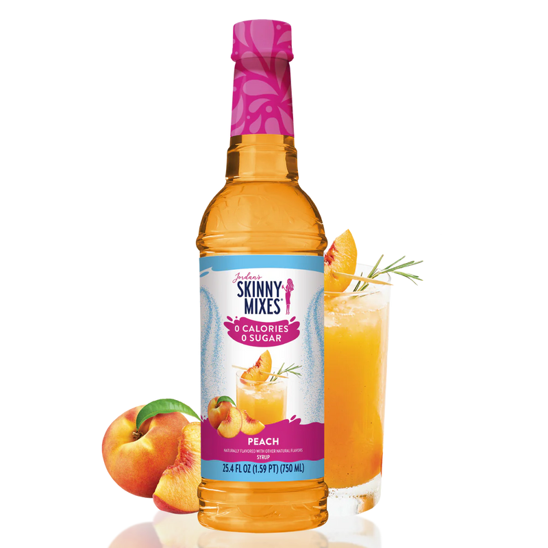Skinny Mixes peach syrup bottle with a glass of peach juice and peaches on a white background