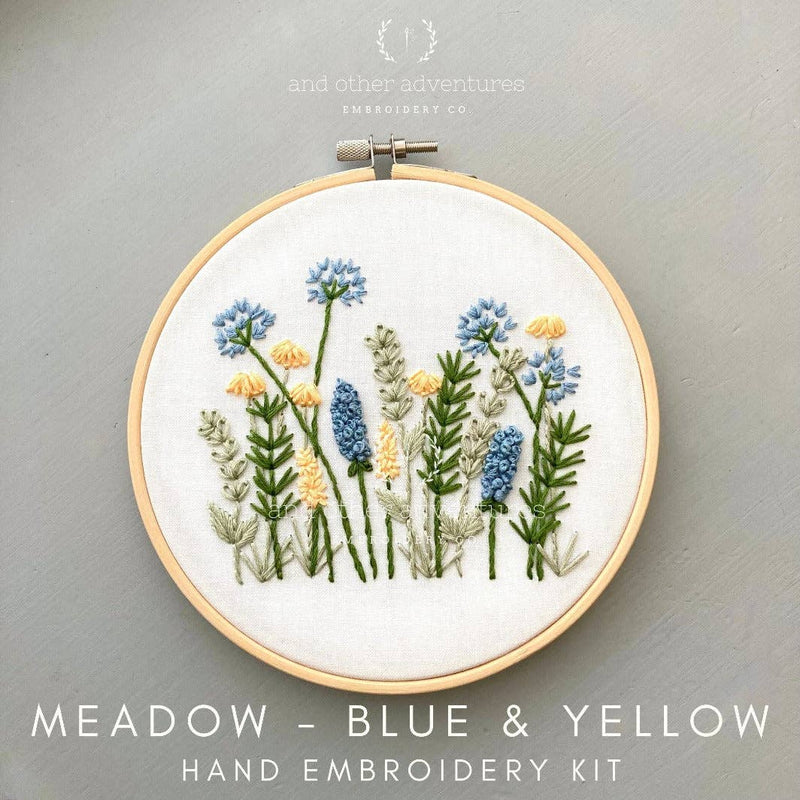 Hand embroidery kit with blue and yellow flowers in a wooden hoop on a gray background.