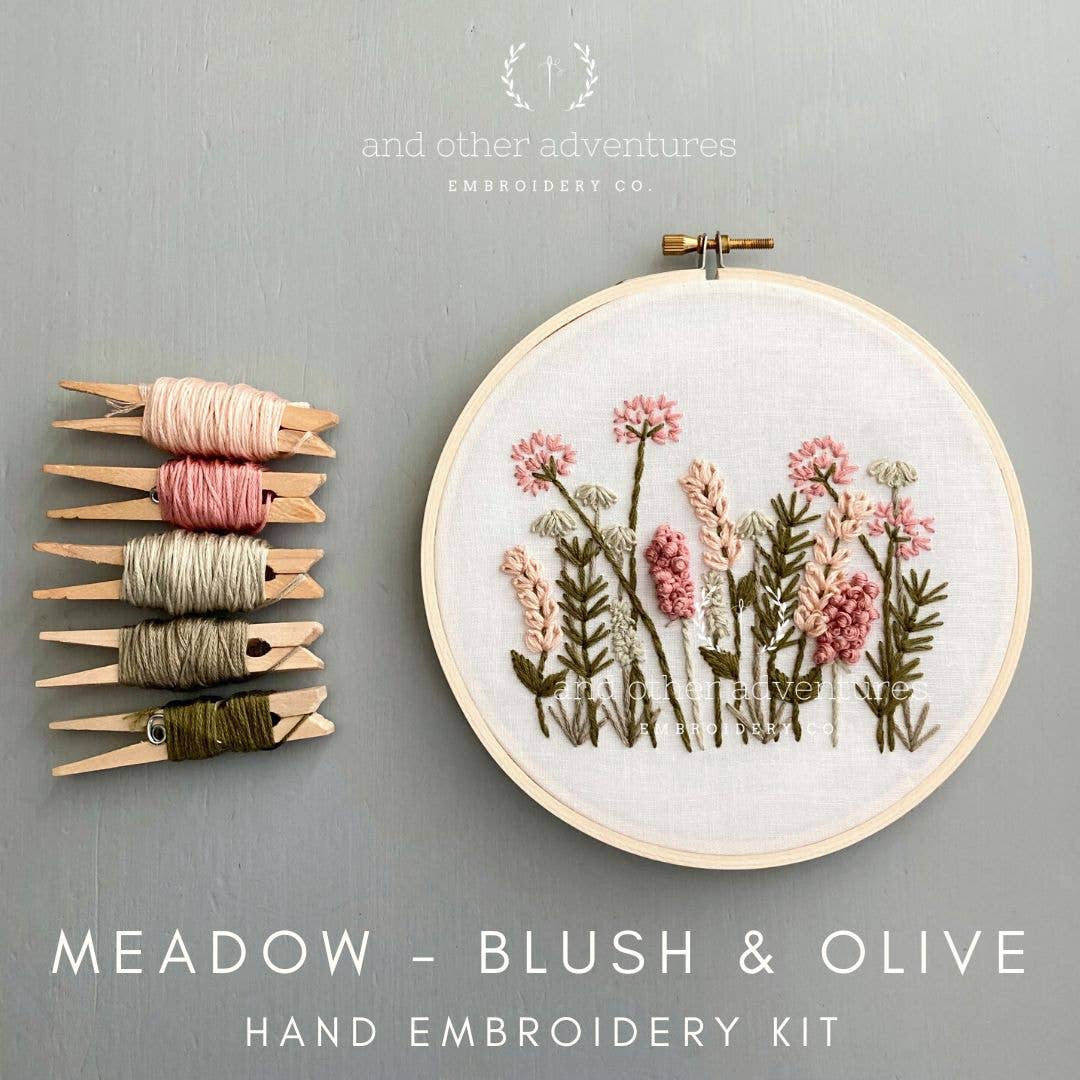 Embroidery hoop with floral design and embroidery thread on a gray background, featuring 'and other adventures embroidery co' branding.