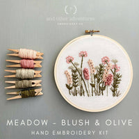 Embroidery hoop with floral design and embroidery thread on a gray background, featuring 'and other adventures embroidery co' branding.