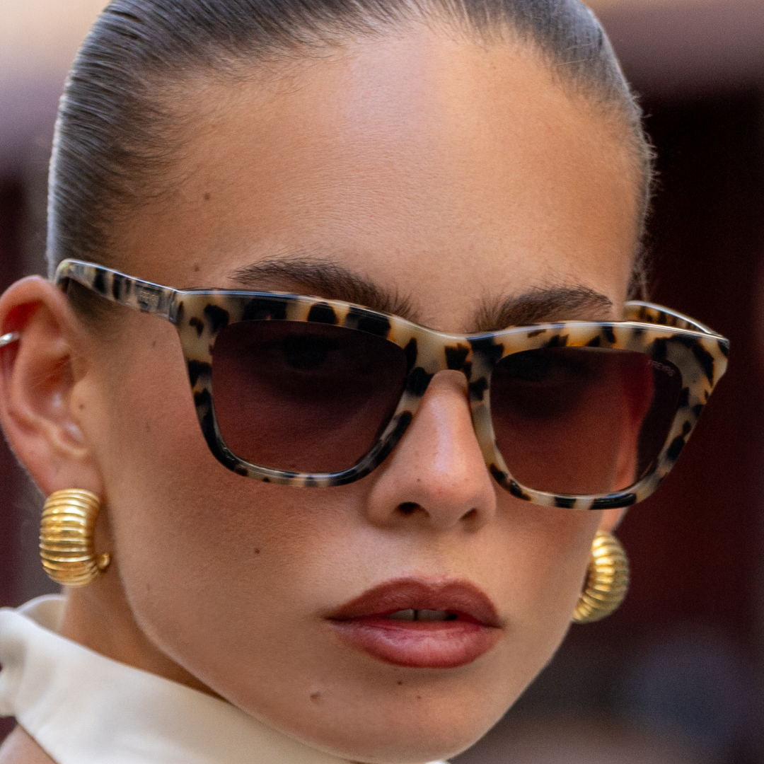 Close-up of a person wearing leopard print sunglasses and gold earrings with a blurred background