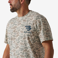Man wearing a camouflage-patterned t-shirt with a logo on a plain background