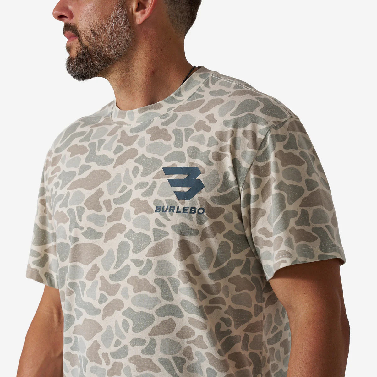 Man wearing a camouflage-patterned t-shirt with a logo on a plain background