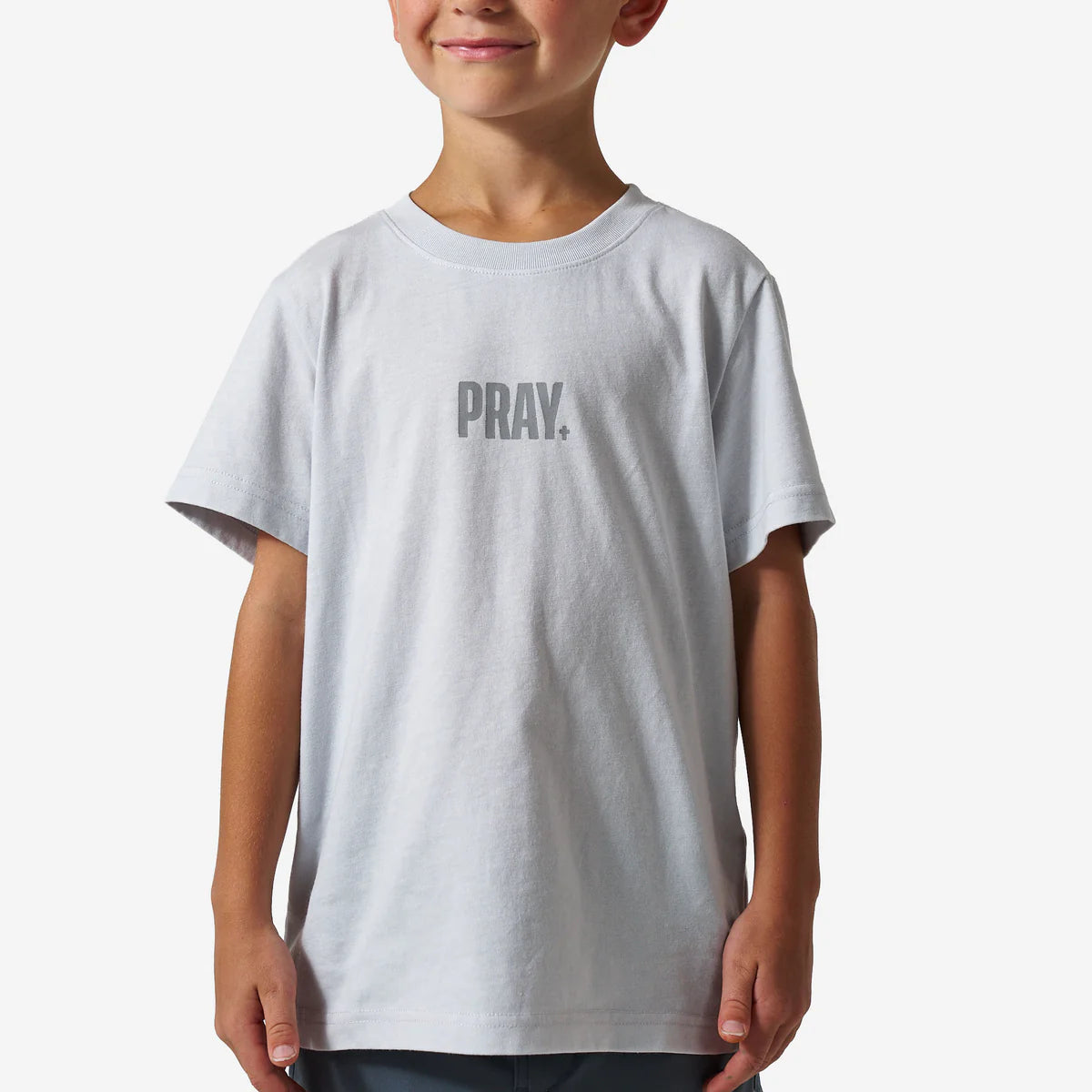 Child wearing a white t-shirt with 'PRAY.' printed on it against a plain background