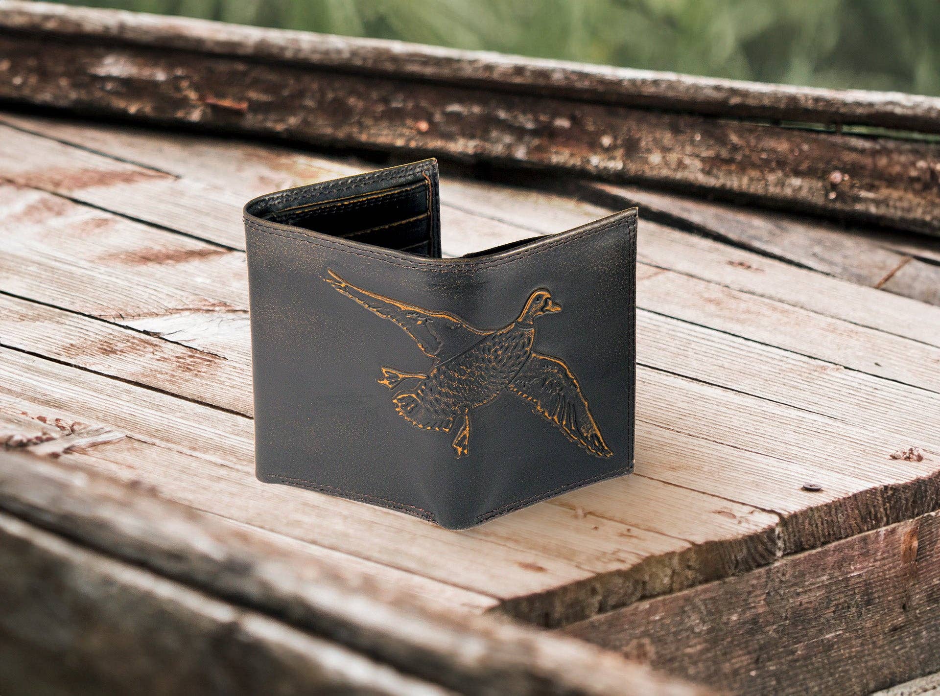 Black leather wallet with a gold duck design on a wooden surface
