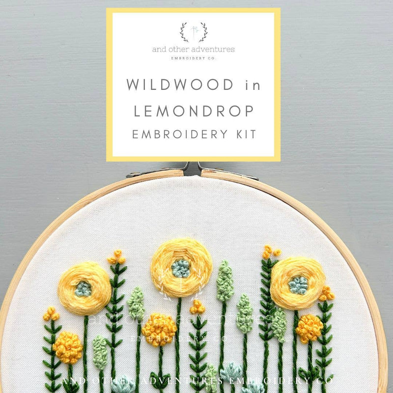 Embroidery hoop with embroidered flowers and leaves, featuring Wildwood in Lemondrop embroidery kit branding.