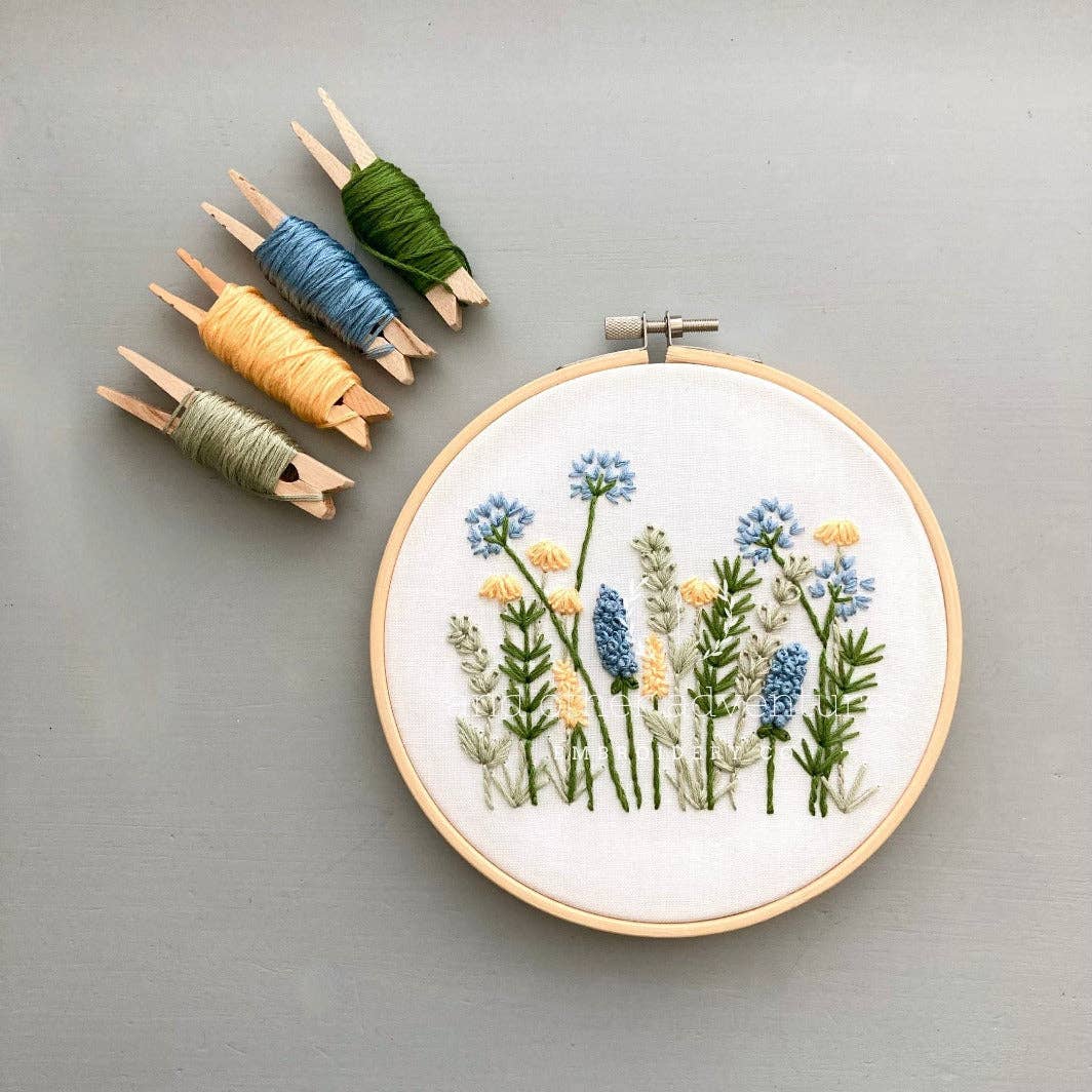 Embroidery hoop with floral design and colorful thread spools on a gray background