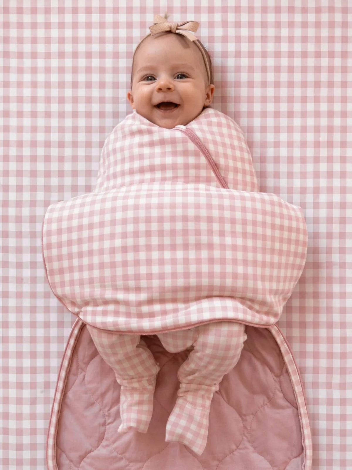 Baby wrapped in a pink checkered blanket on a pink checkered background