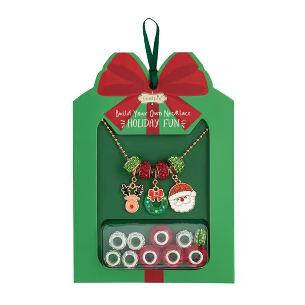A Christmas-themed necklace building kit in a green gift box with a red bow. The kit includes a gold-tone chain necklace with holiday charms (reindeer, wreath, Santa) and several rows of colorful beads inside a clear window at the bottom.