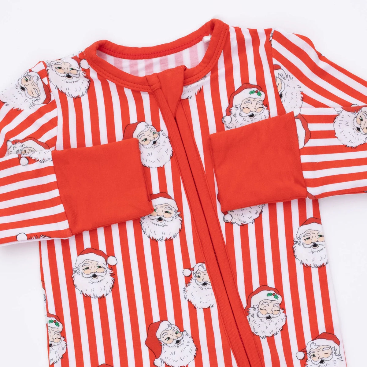 A long-sleeve baby footed sleeper with red and white vertical stripes, featuring a repeating pattern of Santa Claus faces and solid red pocket flaps on a white background.