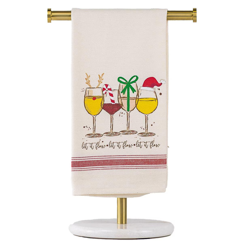 An off-white kitchen towel with a Christmas-themed wine glass illustration and the phrase 'let it flow-let it flow-let it flow' hanging from a gold stand against a white background.