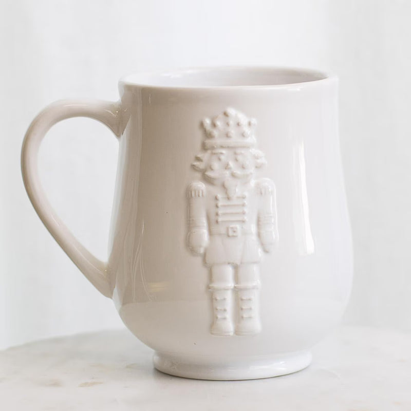 A white ceramic mug with a raised nutcracker figure on the front, set against a clean white background.