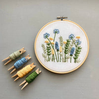 Embroidery hoop with floral design and colorful thread on a gray background