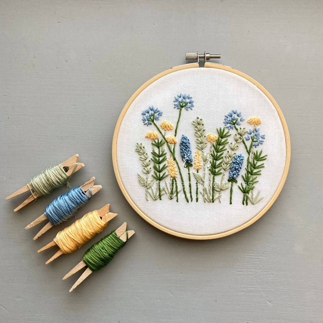 Embroidery hoop with floral design and colorful thread on a gray background