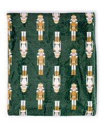 A dark green plush blanket featuring a repeating pattern of gold and white nutcracker figures, shown flat against a white background.