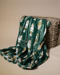 Green blanket with nutcracker pattern draped over a wicker basket on a beige background