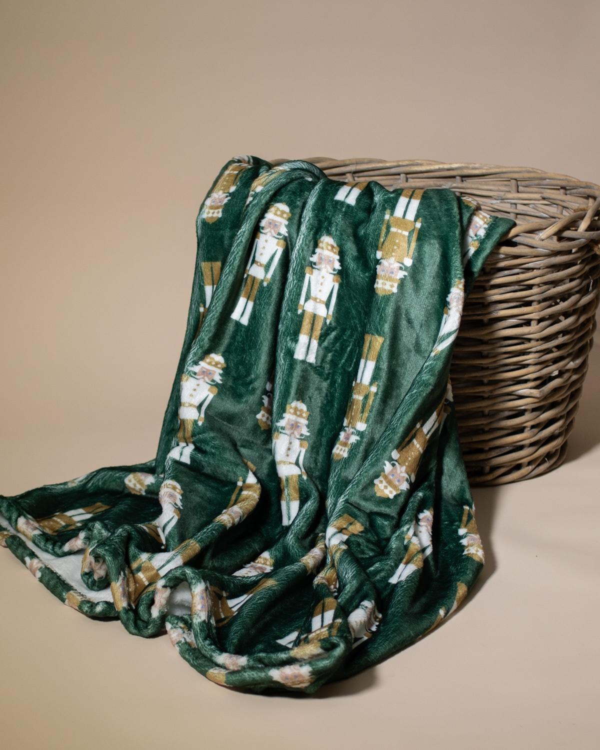 Green blanket with nutcracker pattern draped over a wicker basket on a beige background