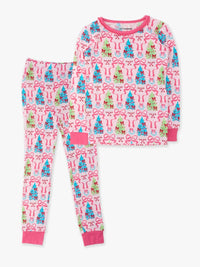A two-piece children's pajama set featuring a long-sleeve top and matching pants with a festive holiday print of Christmas trees, bows, and snowman faces on a light pink background.
