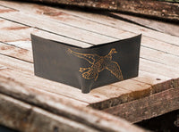 Black leather wallet with a gold embossed duck design on a wooden surface