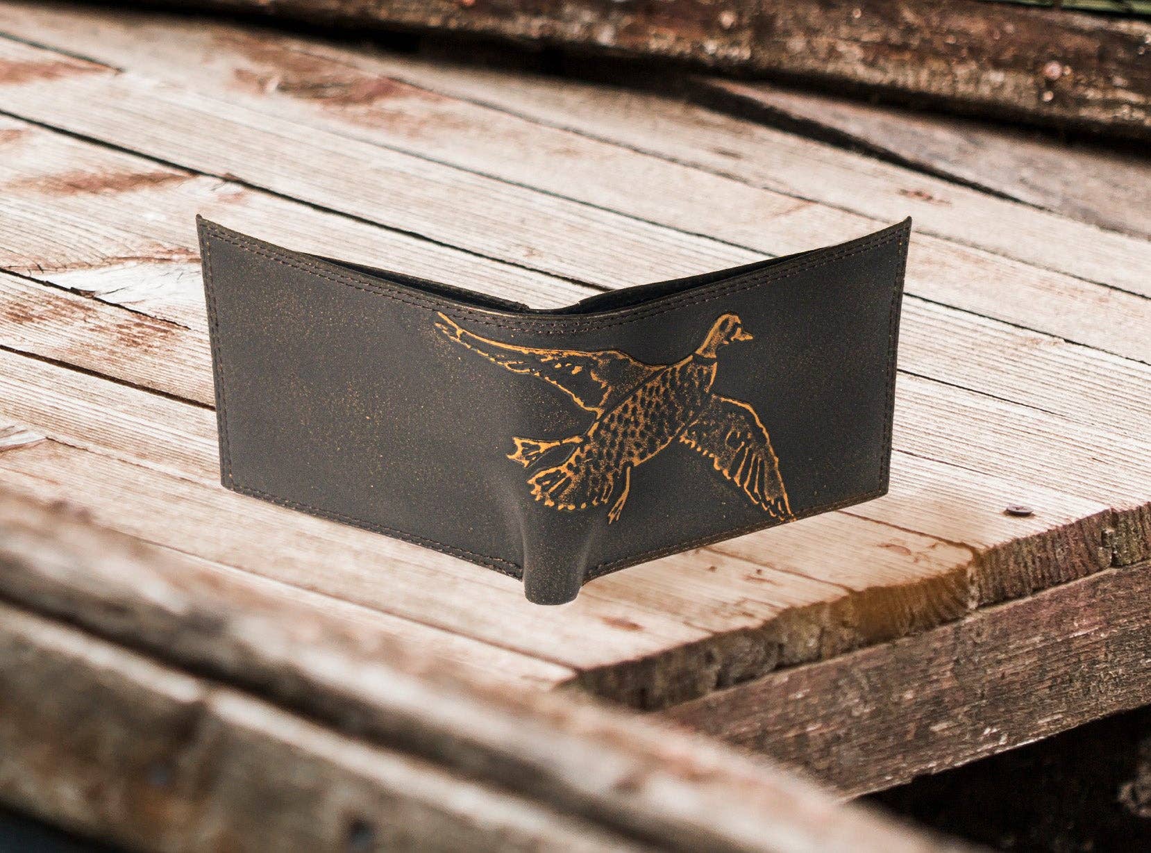Black leather wallet with a gold embossed duck design on a wooden surface