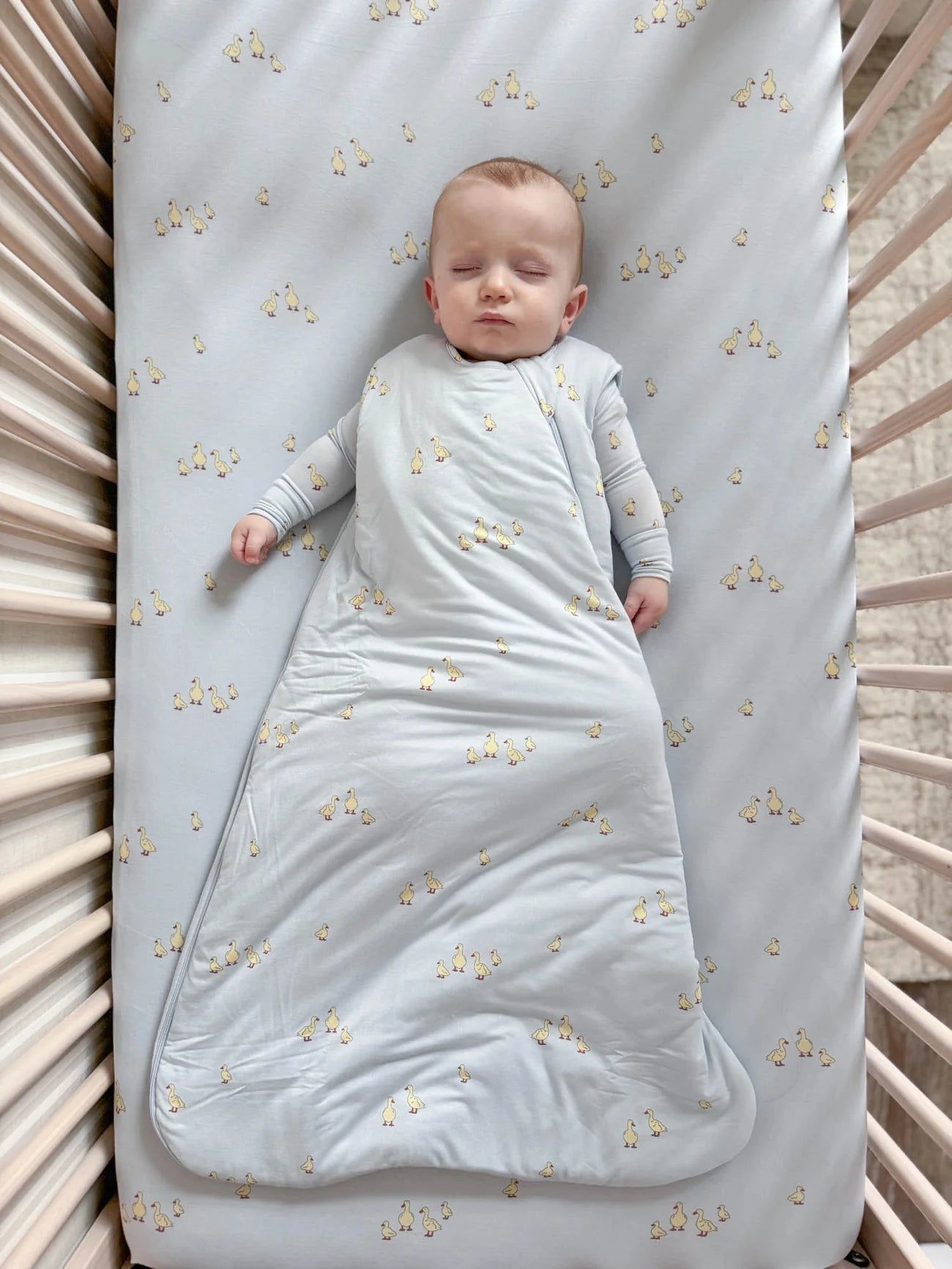 Baby wrapped in a light blue swaddle with star pattern lying on a crib.