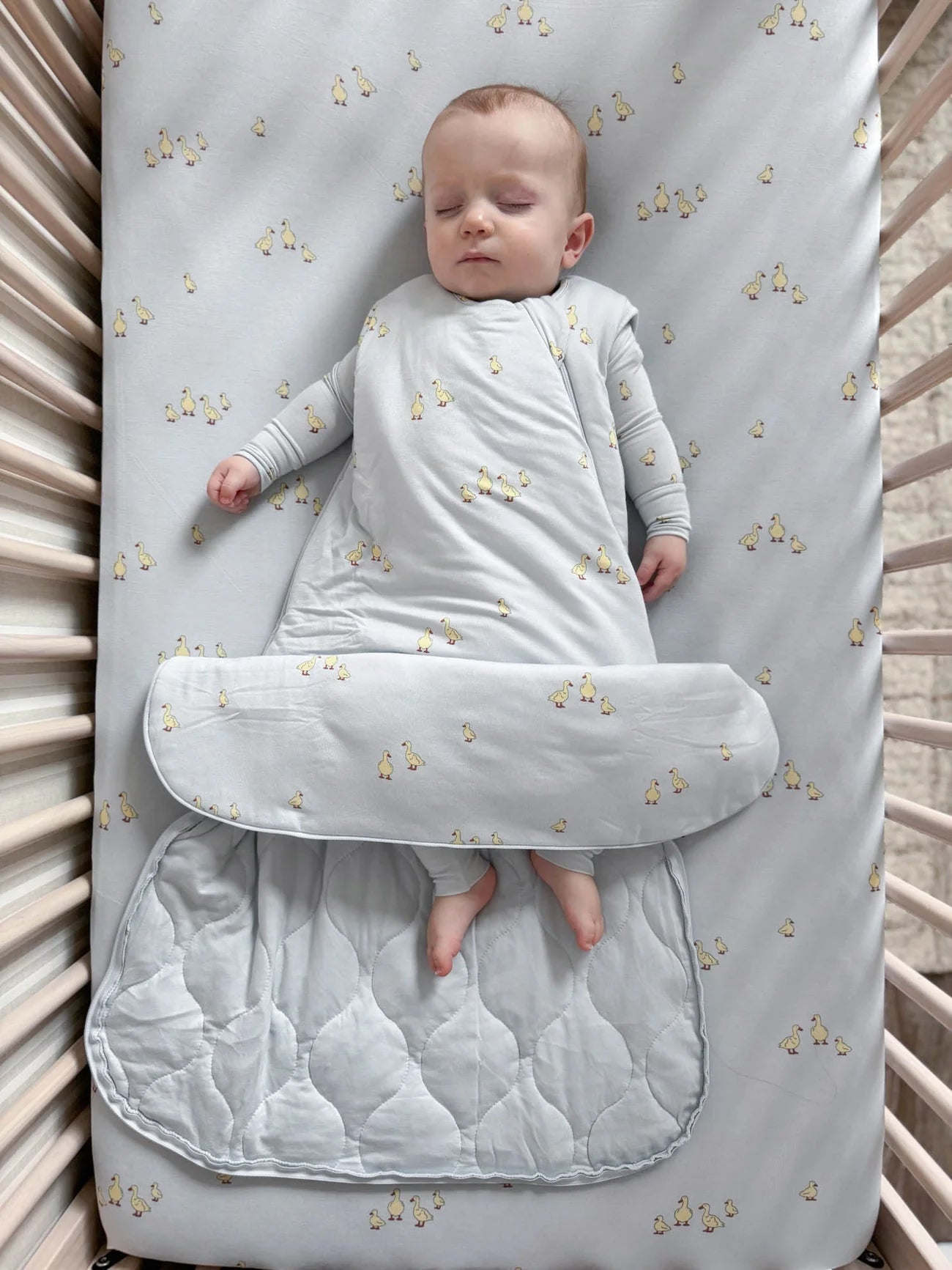Baby swaddled in a light gray blanket with star pattern in a crib.