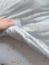 White baby blanket with duck pattern and a hand holding it open.