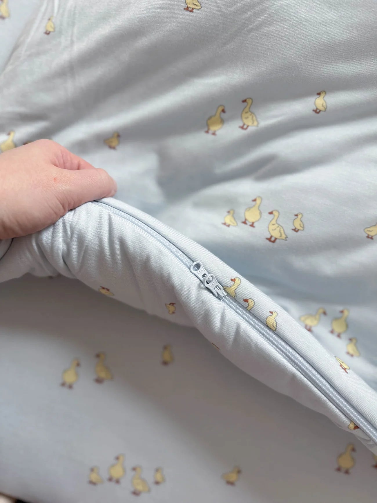 White baby blanket with duck pattern and a hand holding it open.