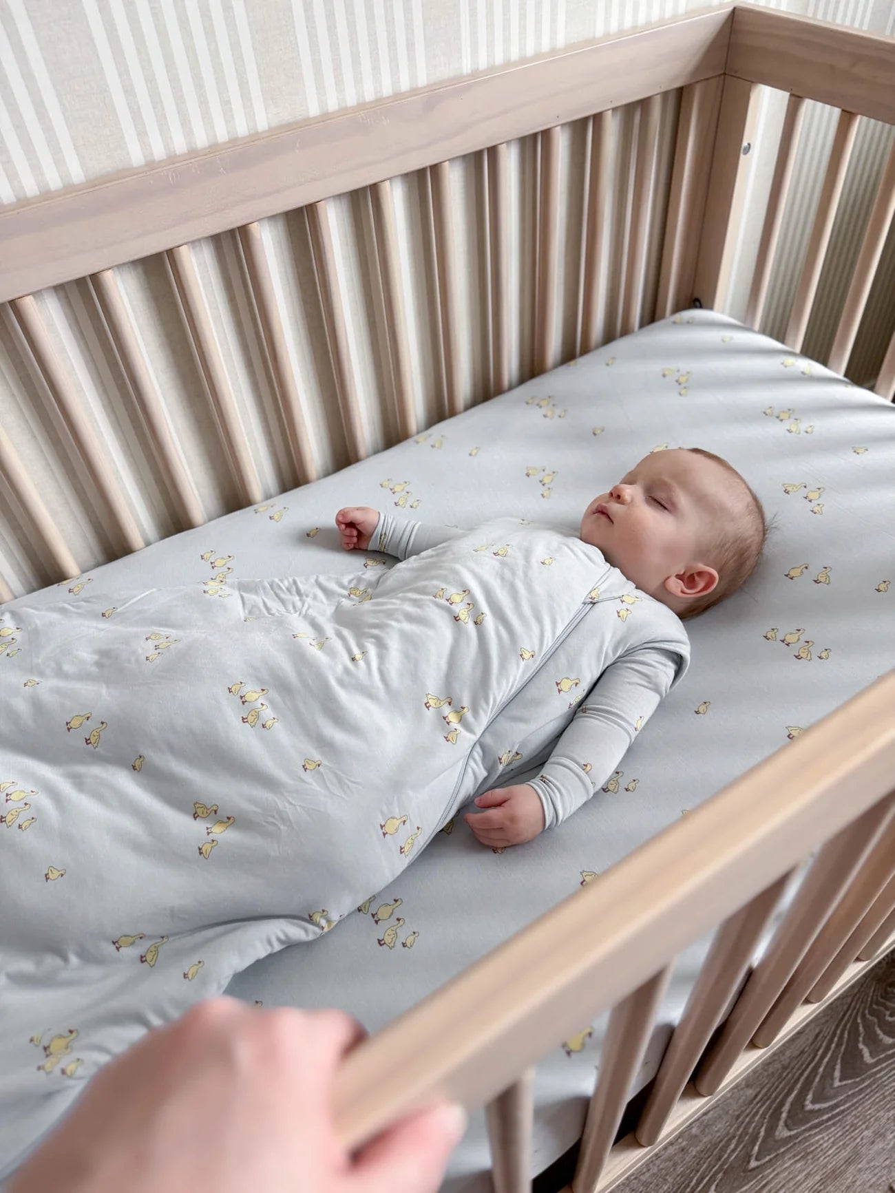 Baby lying in a crib with a gray mattress and floral pattern
