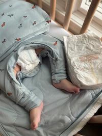 Baby in a crib with a blue blanket and diapers nearby