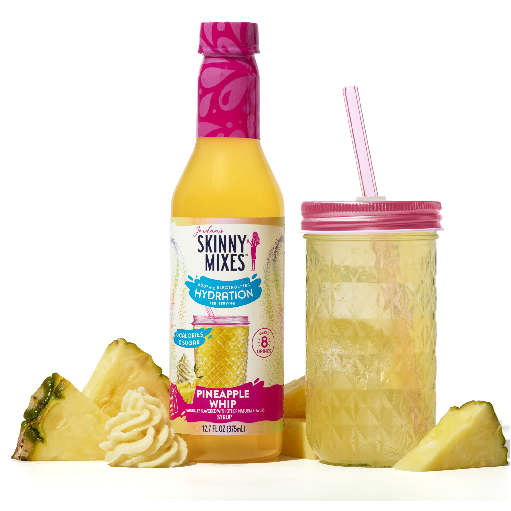 Skinny Mixes Pineapple Whip drink bottle with a pink cap, pineapple slices, and a glass with pink lid and straw on a white background.