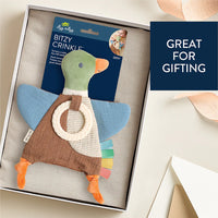 A duck-shaped baby teething toy with a green head, blue wings, brown body, orange beak and feet, a cream ring handle, and colorful fabric tabs along the tail, shown on a white background.