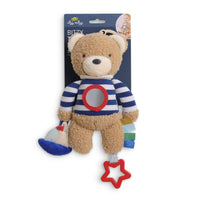 A baby plush toy shaped like a teddy bear wearing a blue and white striped shirt with a red circular patch on the chest. The bear has a blue hat and a red star-shaped teething ring hanging from its tail.