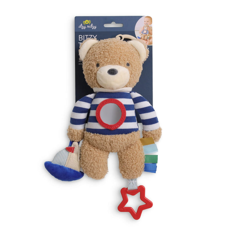 A baby plush toy shaped like a teddy bear wearing a blue and white striped shirt with a red circular patch on the chest. The bear has a blue hat and a red star-shaped teething ring hanging from its tail.