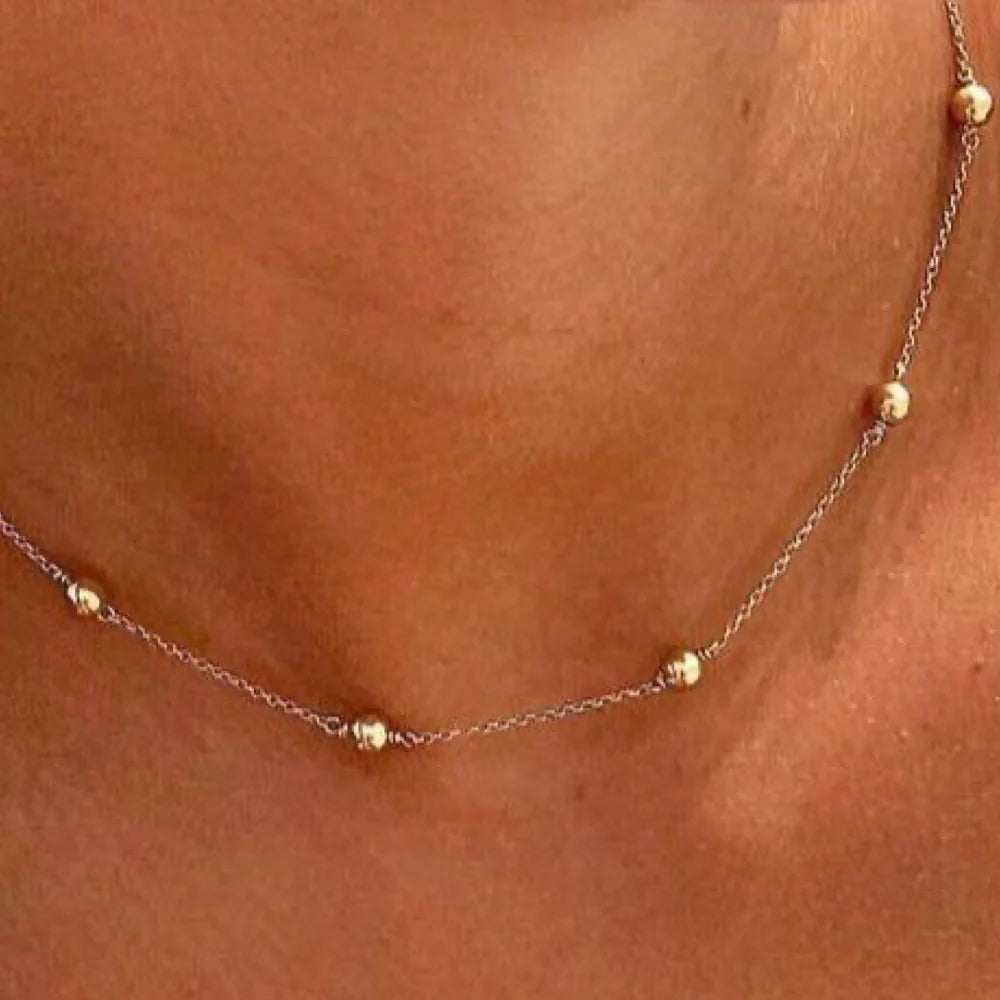 Gold necklace with small beads on a person's neck against a brown background