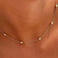 Gold necklace with small beads on a person's neck against a brown background