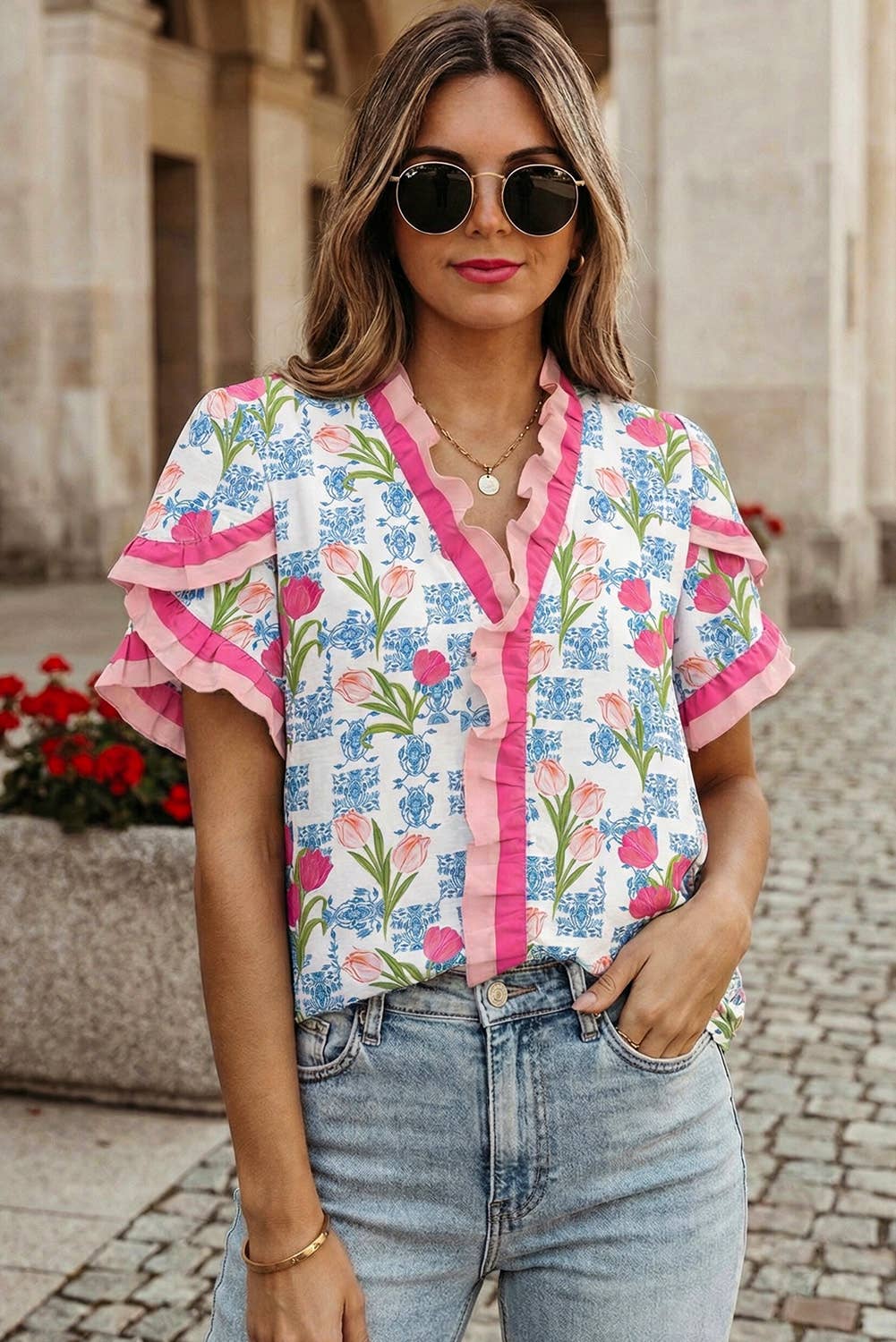 Woman wearing a colorful floral blouse with ruffled sleeves and denim jeans, standing outdoors.