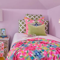 Colorful bedding and pillows on a bed in a room with purple walls.