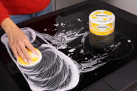 Person cleaning a glass surface with a sponge and Shadazze cleaning product.