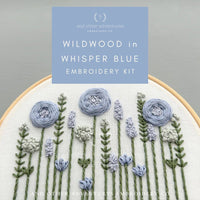 Embroidery kit with floral design and 'Wildwood in Whisper Blue' text on a gray background