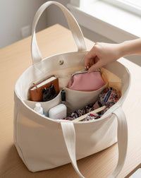 White tote bag with various items on a wooden surface