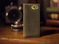 Green leather wallet with a decorative emblem on a wooden surface with vintage camera in the background