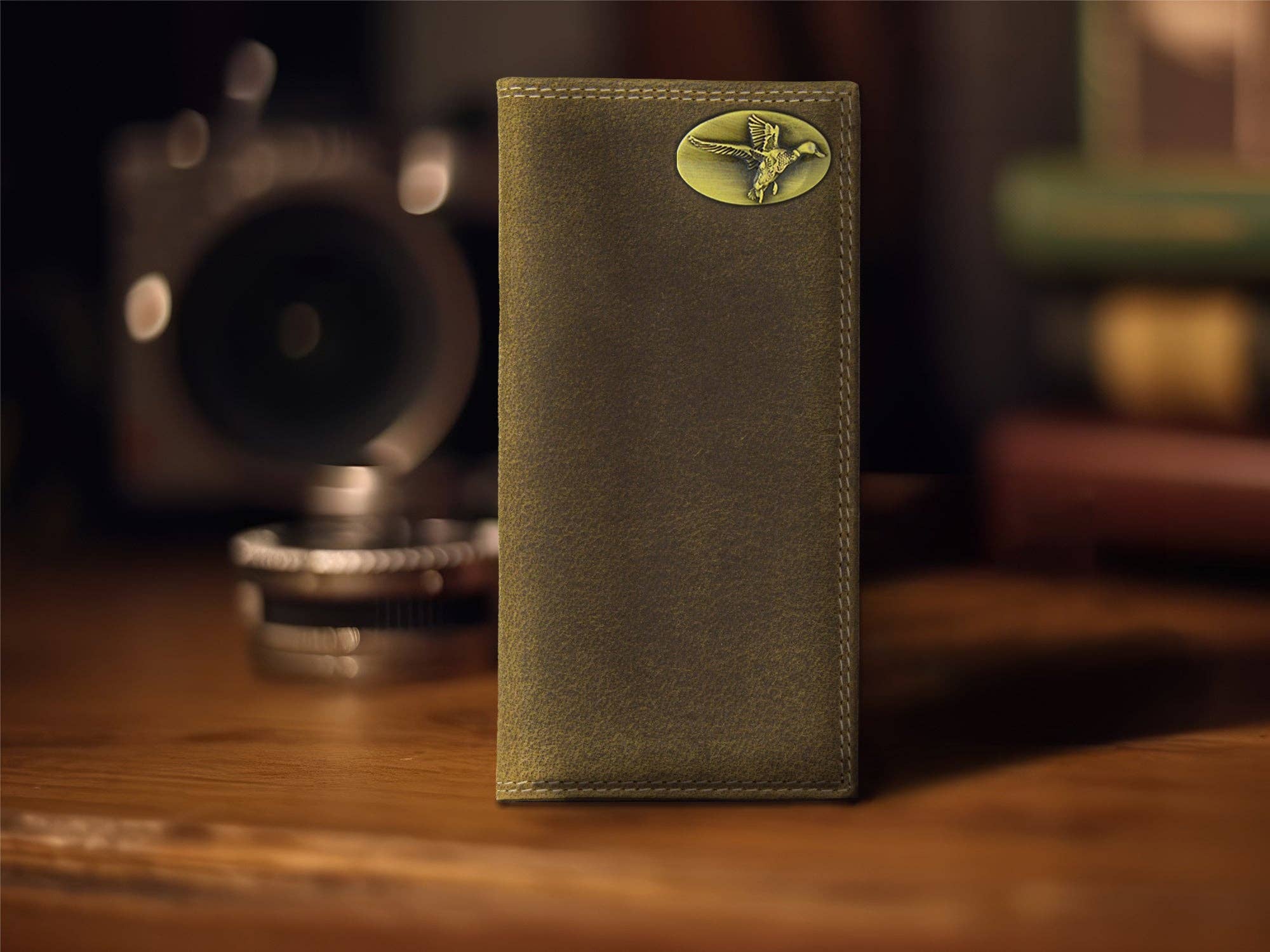 Green leather wallet with a decorative emblem on a wooden surface with vintage camera in the background