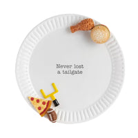 A white ceramic platter with a black printed phrase reading 'Never lost a tailgate' in the center, styled with small food-themed decorations including a chicken leg, hamburger bun, pizza slice, football, and a yellow goal post on a white background.