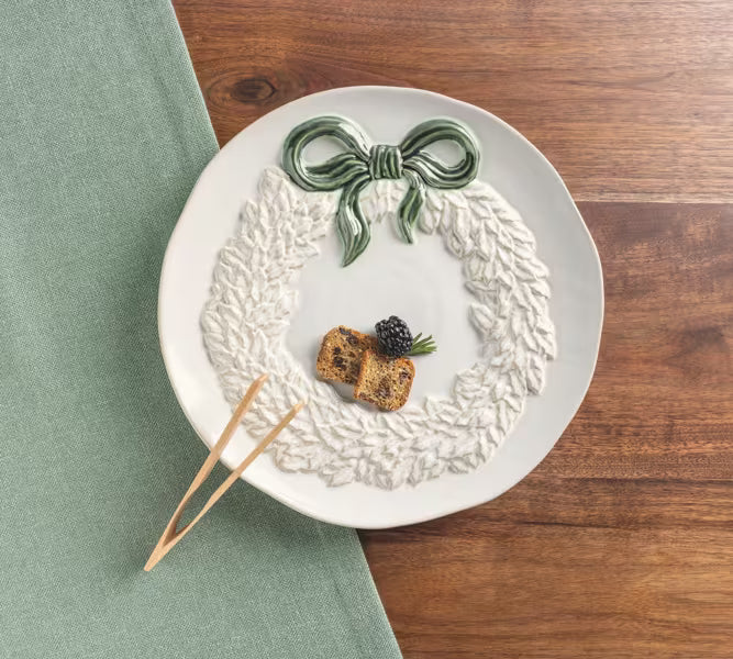 A white ceramic plate with a raised leaf wreath design and a green bow, styled on a wooden table with a green napkin and wooden picks.
