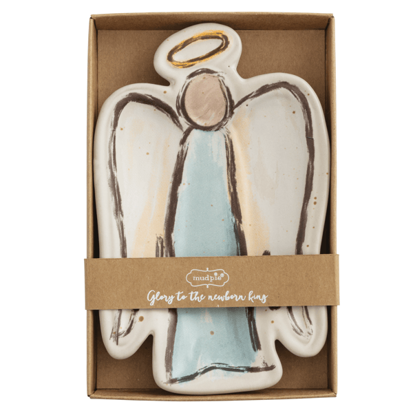 A ceramic angel-shaped cookie or plaque in a brown gift box, featuring an off-white body with a light blue dress, dark brown outline details, and a gold halo at the top. A kraft paper band around the box reads 'mealtime' and 'Glow to the newborn king'.