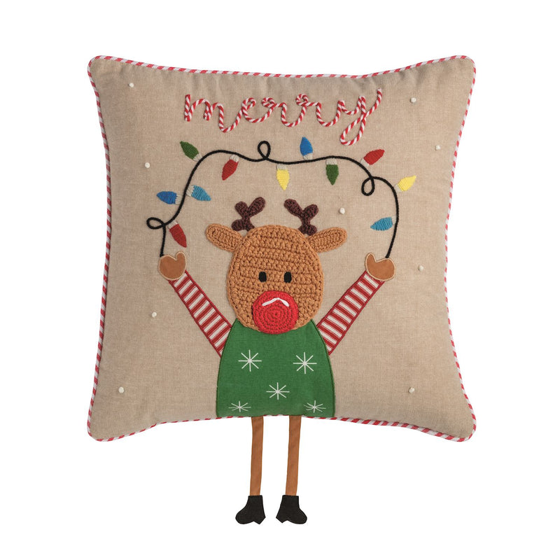 A square beige throw pillow featuring a crocheted reindeer holding a string of multicolored Christmas lights, with 'merry' stitched above in red and white candy canes. The pillow has red-and-white striped piped edges and is shown against a plain white background.