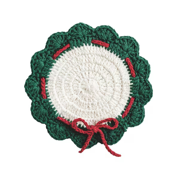A crocheted holiday wreath-shaped doily or coaster with a dark green scalloped border, a white center, and red stitched accents and bow details, shown on a plain white background.