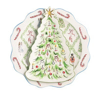 A decorative ceramic Christmas tree-shaped plate or dish placed on top of a scalloped round plate with holiday illustrations including candy canes, green garlands, and a nutcracker, shown on a white background.