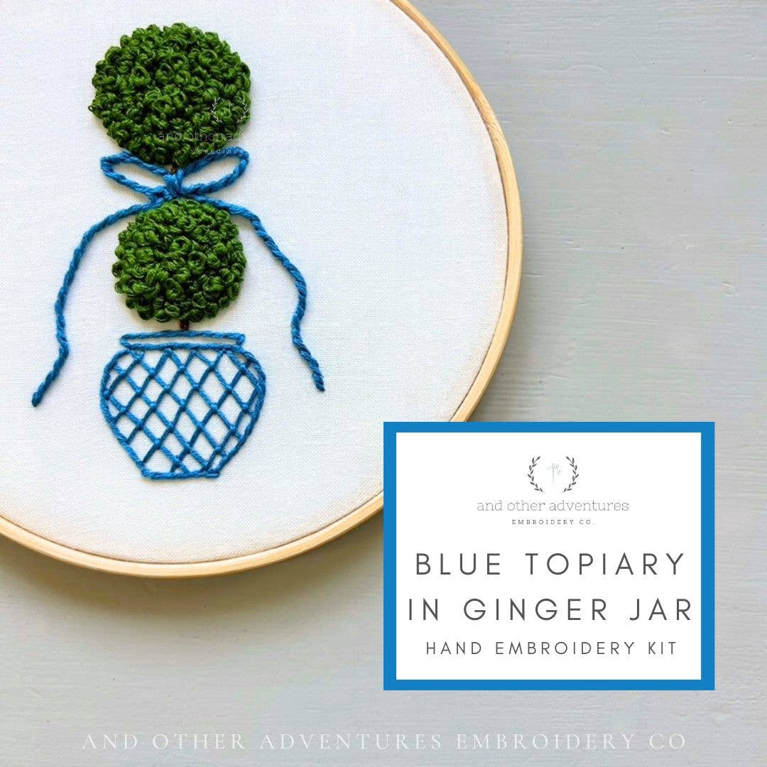 Embroidery hoop with blue topiary design and text about embroidery kit on a light gray background